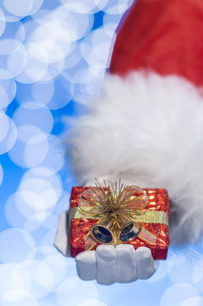 圣诞老人的手拿着一个红色包装的小礼物在蓝色背景和白色散焦图片下载