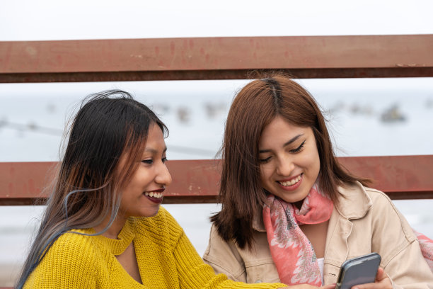 两个朋友在户外共享手机的裁剪照片图片下载