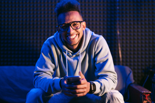 卷毛男人戴着眼镜，拿着智能手机坐在沙发上图片下载