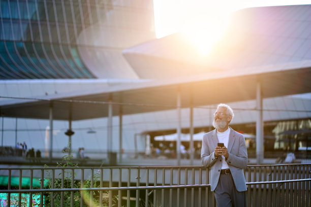 快乐的老商人站在城市的户外用手机。图片下载