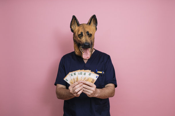戴着乳胶狗头面具的年轻人手里拿着粉红色背景上的钱图片下载