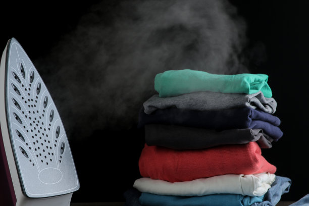 丁香铁释放蒸汽和一堆衣服在黑色的背景。熨烫衣服。家用电器。图片下载