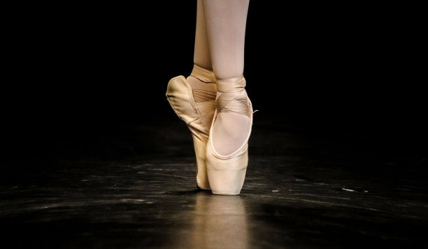 一个芭蕾舞演员的脚在一个黑色的舞池上跳舞的特写图片下载