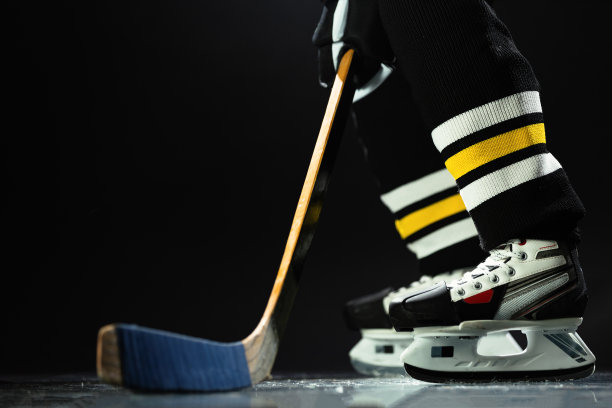 曲棍球运动员穿着运动服和溜冰鞋，手里拿着棒子站着。图片下载