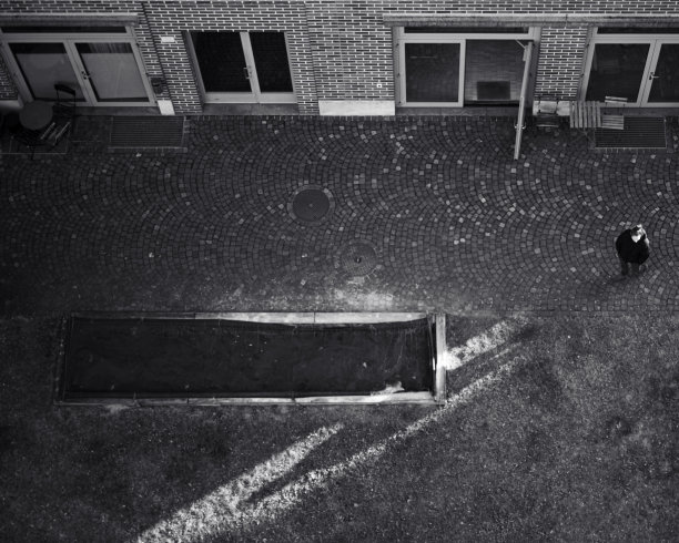 一个人独自站在一幢大楼门口附近的空院子里的航空灰度照片图片下载