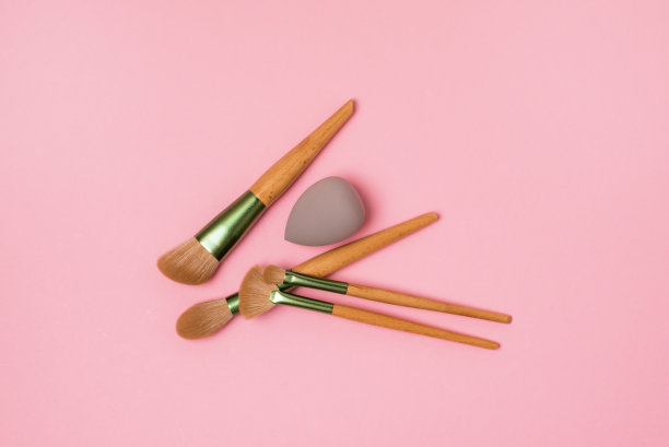 化妆艺术家的工具在粉色背景刷粉灰色海绵遮瑕膏和基础俯视图图片下载