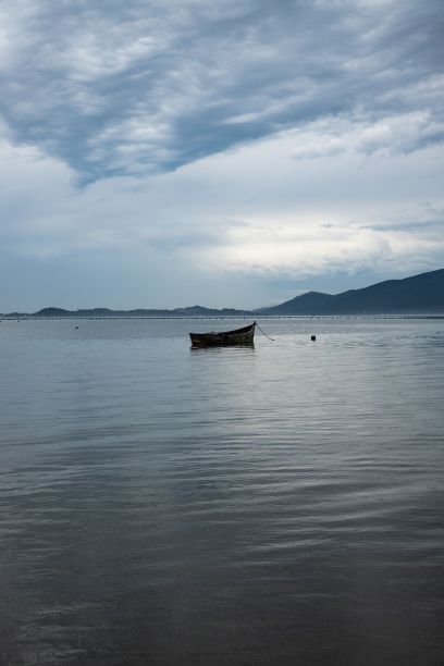在多云的天空下，垂直拍摄湖中的木制渔船图片下载