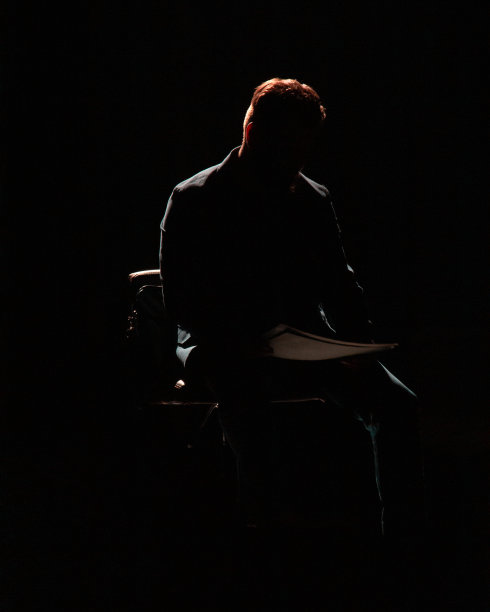 在一间黑屋子里，一个男人坐在椅子上看报纸的剪影图片下载