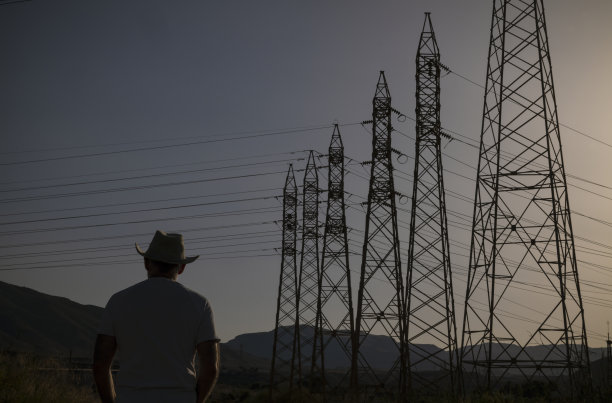 夕阳西下，戴牛仔帽的成年男子的剪影，映衬着发射塔图片下载
