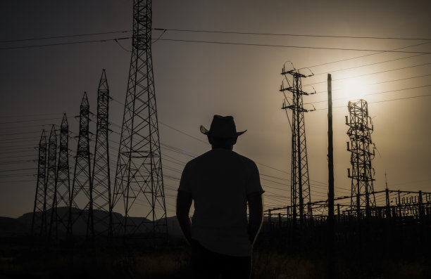 夕阳西下，戴牛仔帽的成年男子的剪影，映衬着发射塔图片下载