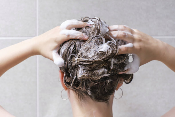 后视图，一个女孩在灰色瓷砖背景上用洗发水洗头。图片下载