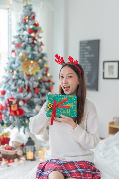 肖像照片的年轻美丽友好的亚洲女性与可爱的圣诞发带愉快地分发礼盒与一个漂亮的装饰圣诞树在背景图片下载