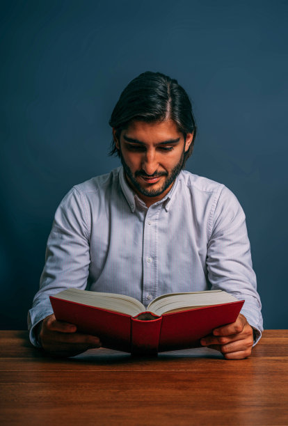 西班牙绅士，留着胡子，坐在木桌上读着红书图片下载