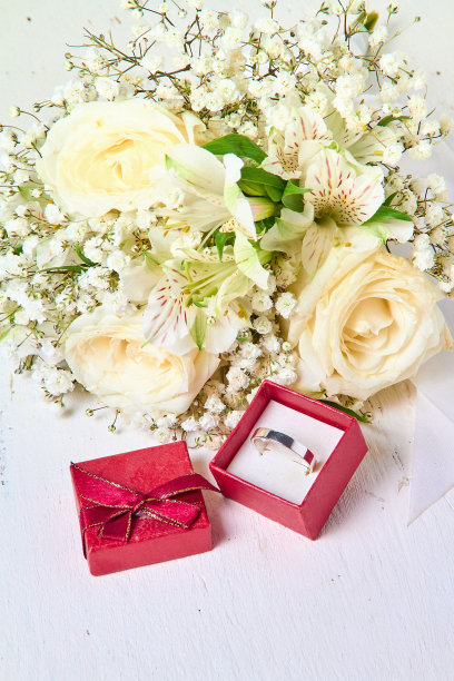银色戒指在红色礼品盒和花束在白色纹理木制背景，节日图片下载