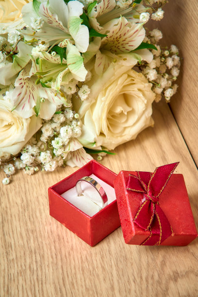 红色礼盒里的白金戒指，木制背景上的一束白花，节日图片下载