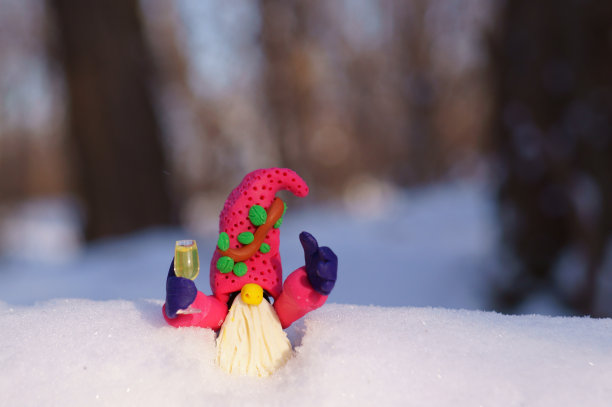 一个用橡皮泥做成的小矮人，手里拿着一杯香槟，背景是皑皑白雪。图片下载