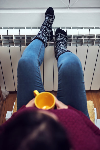 女人在寒冷的冬天给脚取暖，拿着咖啡茶杯，能源和天然气危机，寒冷的房间，供暖问题。图片下载