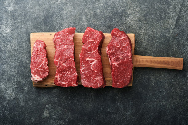 生的牛排。顶部刀片牛排在木烧板上与香料，迷迭香，蔬菜和食材烹饪在黑色背景。前视图。副本的空间。图片下载