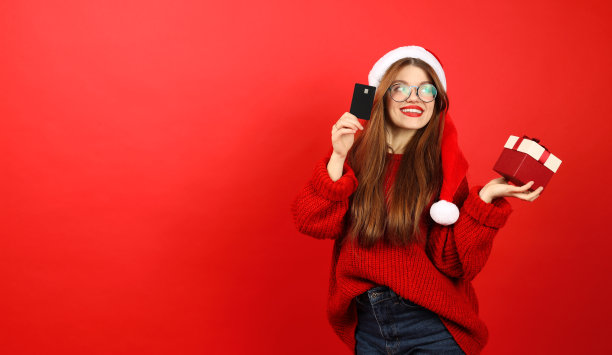 快乐的年轻女子与礼物和信用卡在她的手在一个红色的背景，圣诞购物。图片下载