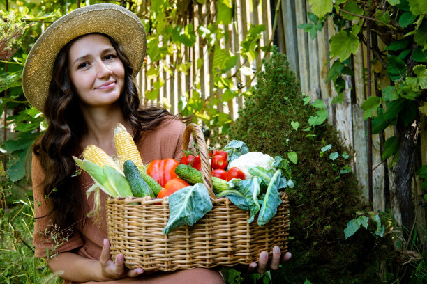 美丽的白种人妇女戴草帽和亚麻衣服在花园里装满蔬菜作物的篮子。秋收和素食有机收获作物。图片下载