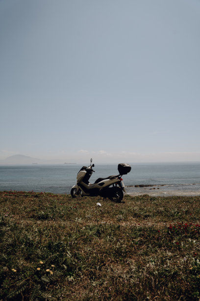 在西班牙塔里法，在蔚蓝无云的天空下，摩托车停在海边的一个长满草的小山上图片下载