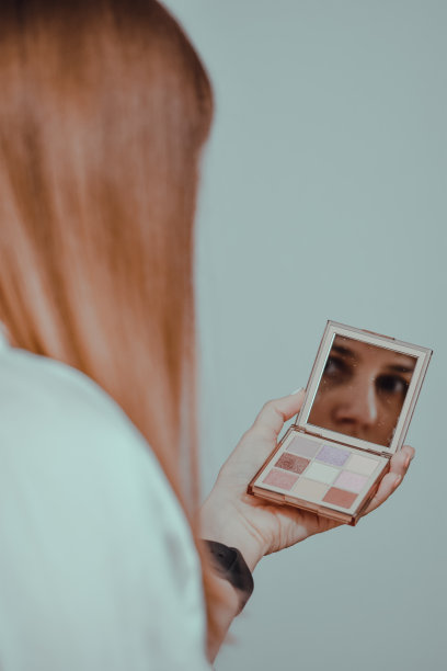 一个年轻的白人女性看着一面小镜子的垂直镜头图片下载