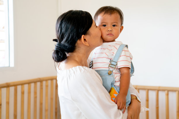 亚洲母亲抱着和亲吻她的小男孩，孩子看着镜头，他们呆在托儿所或学校里，在家庭中有着良好的关系和爱的纽带。图片下载