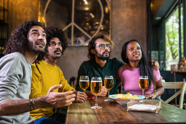 一群多种族的朋友坐在酒吧里满怀期待地观看体育比赛。图片下载