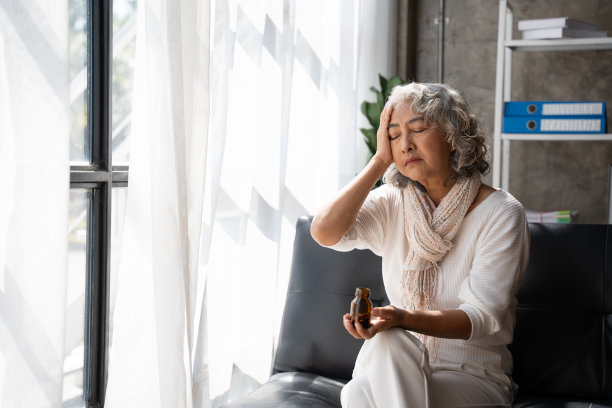悲伤抑郁的中年妇女坐在家里的沙发上，低头摸着额头，孤独和痛苦的概念。图片下载