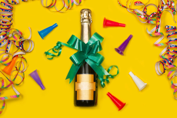 一瓶香槟酒，黄色背景，绿色蝴蝶结，彩色花环和玩具小号图片下载