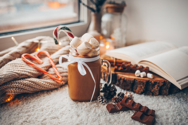 一杯有棉花糖的可可，巧克力，一本打开的书，在舒适的家庭气氛的窗台上的灯。圣诞节的美学图片下载