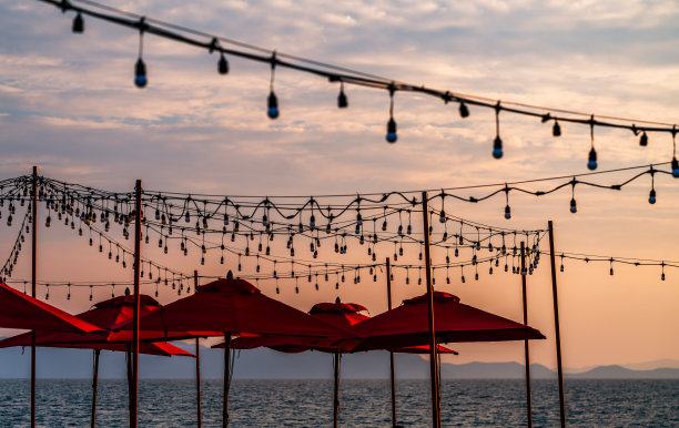 美丽的日落景象与许多红色的伞海滩和派对灯泡挂在空中，五颜六色的日落天空。图片下载