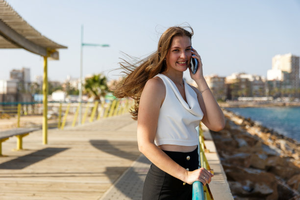 一位年轻时尚的女性在城市的堤岸上用智能手机交流，“在大自然中休息和工作，在海边。图片下载