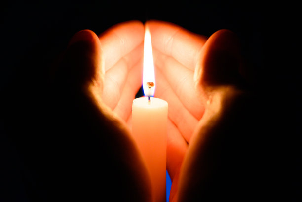 在黑暗的黑色背景下，在手掌里燃烧的蜡烛图片下载