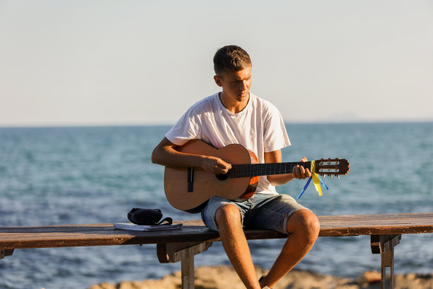一个年轻时髦的小伙子在海边的河堤上弹着吉他，音乐和放松的概念图片下载
