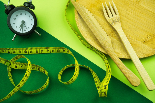 顶视图的一个木制盘子和餐具，一个闹钟，和一个测量带在一个彩色的背景图片下载