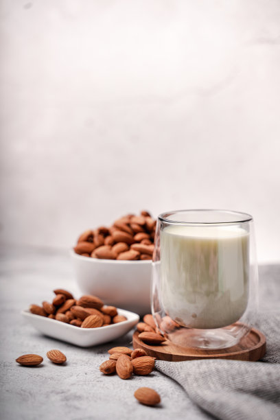 一杯杏仁奶与杏仁籽白色混凝土背景。图片下载