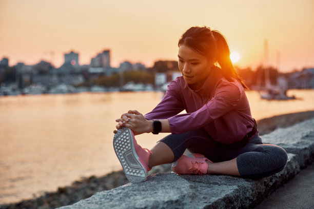 年轻的亚洲运动员在码头上伸展她的腿日落。图片下载