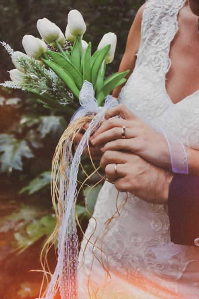 新娘和新郎拿着优雅的现代秋季婚礼花束前面的白色婚纱。背景中可以看到新娘和新郎的结婚戒指图片下载