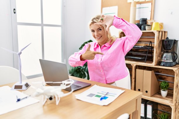 年轻的白人妇女在办公室工作，微笑着做框架的手和手指与快乐的脸。创意和摄影概念。图片下载