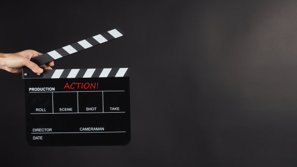 手握黑色背景上的黑色拍板。它有文字和行动。图片下载