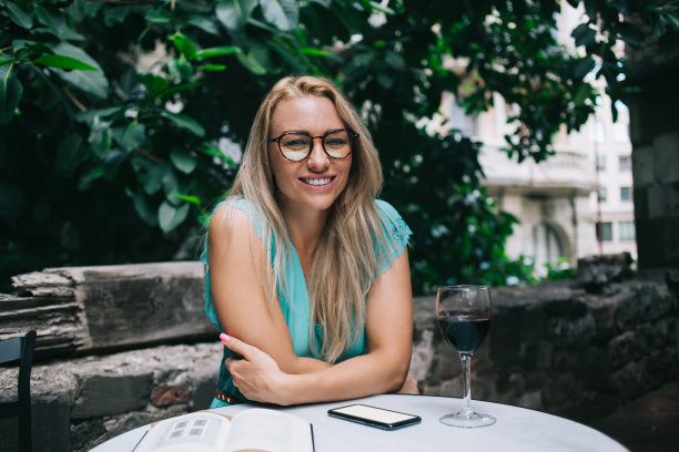 画像快乐的女人在时髦的眼镜为眼睛矫正微笑的相机在休闲时间喝红酒和计划组织在街头自助餐厅，休息的概念图片下载