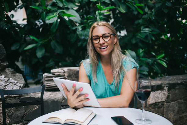画像快乐的女记者30岁手拿平板电脑在街头咖啡馆的酒时间对着镜头微笑，成功的女人戴眼镜享受休闲与现代科技图片下载