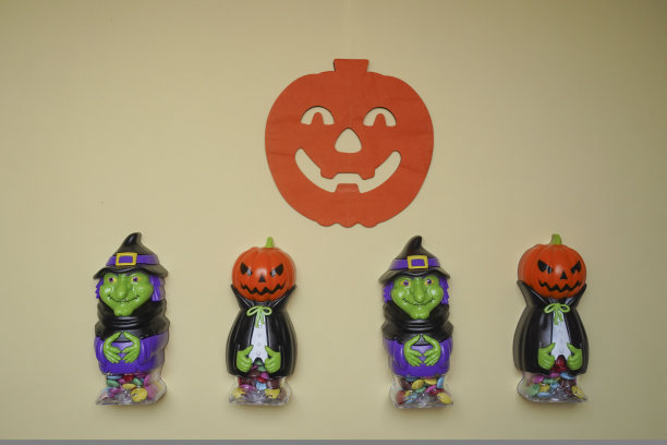 可爱的角色在怪物服装。可怕的万圣节小雕像站在一个明亮的背景上，后面挂着可怕的南瓜。万圣节的概念。节日装饰，玩具和娱乐图片下载