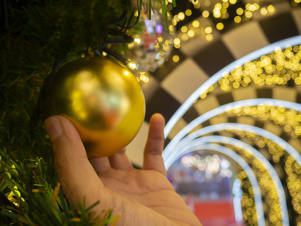 女人的手用球和玩具装饰圣诞树，后面有柔和的灯光模糊图片下载