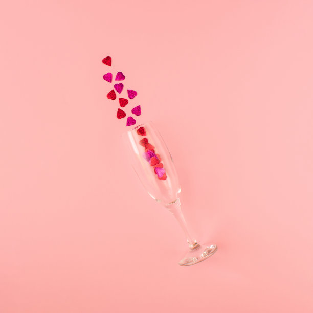 创意组成的香槟杯与闪亮的心形闪光对粉红色的背景。简约的情人节庆祝概念。图片下载