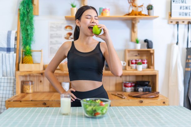 年轻美丽的亚洲女性女士的照片在运动服快乐地享受吃青苹果，喝牛奶和吃沙拉与樱桃番茄在她的房子的饮食和减肥健康的生活方式图片下载