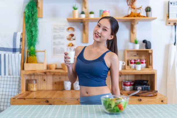 年轻美丽的亚洲女性女士的照片在运动服快乐享受喝牛奶和吃沙拉与樱桃番茄在她的房子的厨房节食和减肥健康的生活方式图片下载
