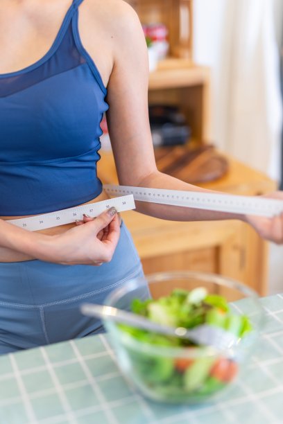 近距离的照片一个年轻美丽的亚洲妇女女士穿着运动服快乐做腰测量检查她的训练锻炼和饮食结果。她家厨房桌上的樱桃番茄沙拉是为了减肥和健康的生活方式图片下载