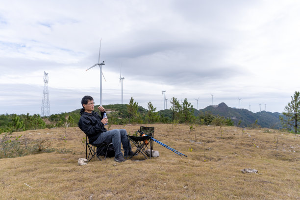 一个中年男子坐在户外的折叠桌椅上喝酒图片下载